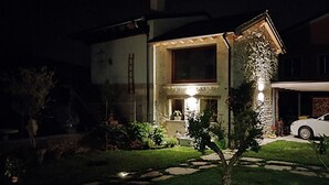 Ein Haus mit einer Steinfassade, einem sichtbaren Schornstein und einem gut beleuchteten Eingangsbereich bei Nacht.