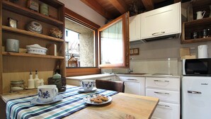 Eine kompakte Küche mit weißen Schränken, einer eingebauten Mikrowelle und einem kleinen Kühlschrank. Über der Spüle befindet sich ein Fenster, und die Küche verfügt über einen Holztisch mit gestreifter Tischdecke.