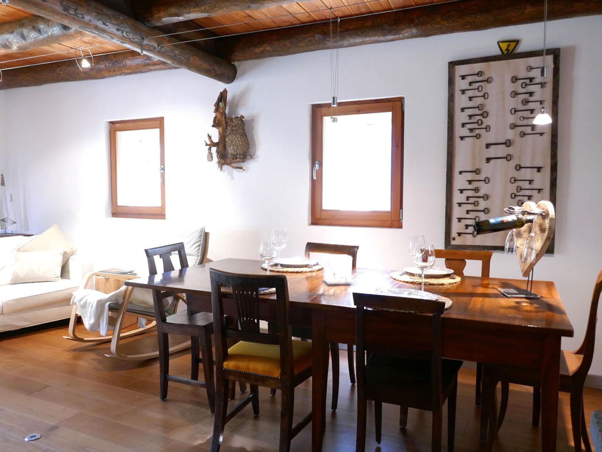 Un comedor con mobiliario de madera, un ventanal grande y un panel con llaveros.