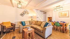 Een gezellige woonkamer met een bank, fauteuil en een houten salontafel. In de achtergrond is een eethoek met een tafel en stoelen zichtbaar.
