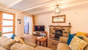 Een woonkamer met een zithoek, een televisie, een open haard en een stenen muur.