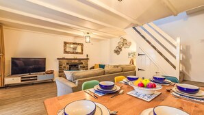 Een moderne woonkamer met een open haard, een bank, een eettafel gedekt met blauwe en witte borden, en een trap naar een bovenverdieping.