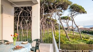 Un balcón con una mesa para dos personas, con vista a un jardín con árboles altos y una zona residencial.