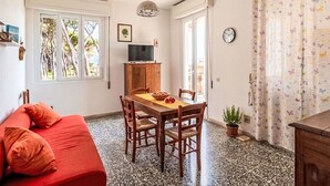 Una habitación acogedora con un sofá rojo, una mesa de comedor de madera con sillas, un televisor sobre un mueble de madera y una ventana con vistas a árboles.