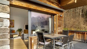 A wooden exterior with a sliding glass door leading to an interior with a table and chairs, a potted plant, and a view of the outdoors. - Cozy Apartment Above the Rooftops of Jenbach (Jenbach)