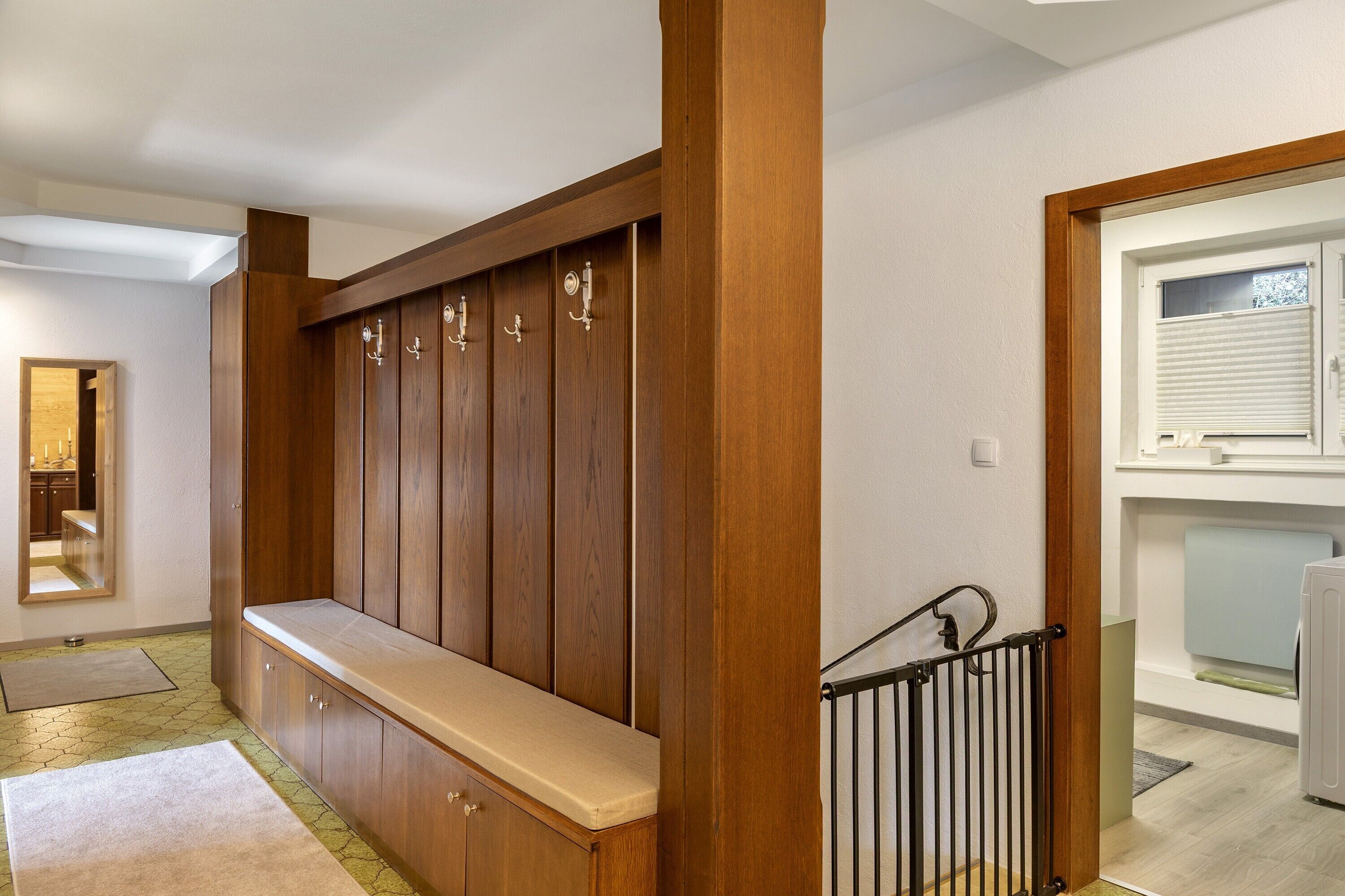A wooden bench with storage cabinets, a mirror, and a staircase with a metal railing.