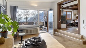 A modern living room with a large window, a fireplace, a dining area, and a staircase leading to an upper floor. - Cozy Apartment Above the Rooftops of Jenbach (Jenbach)