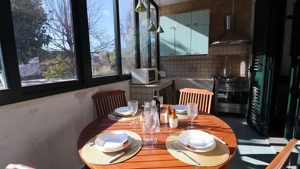 Zona pranzo con tavolo rotondo in legno apparecchiato per quattro persone, con piatti, bicchieri e posate.