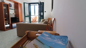 Un soggiorno con un divano, una sedia in legno, una televisione e una libreria.