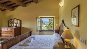 Un dormitorio con cama, cómoda, ventana con vistas, lámpara y un cuadro en la pared.