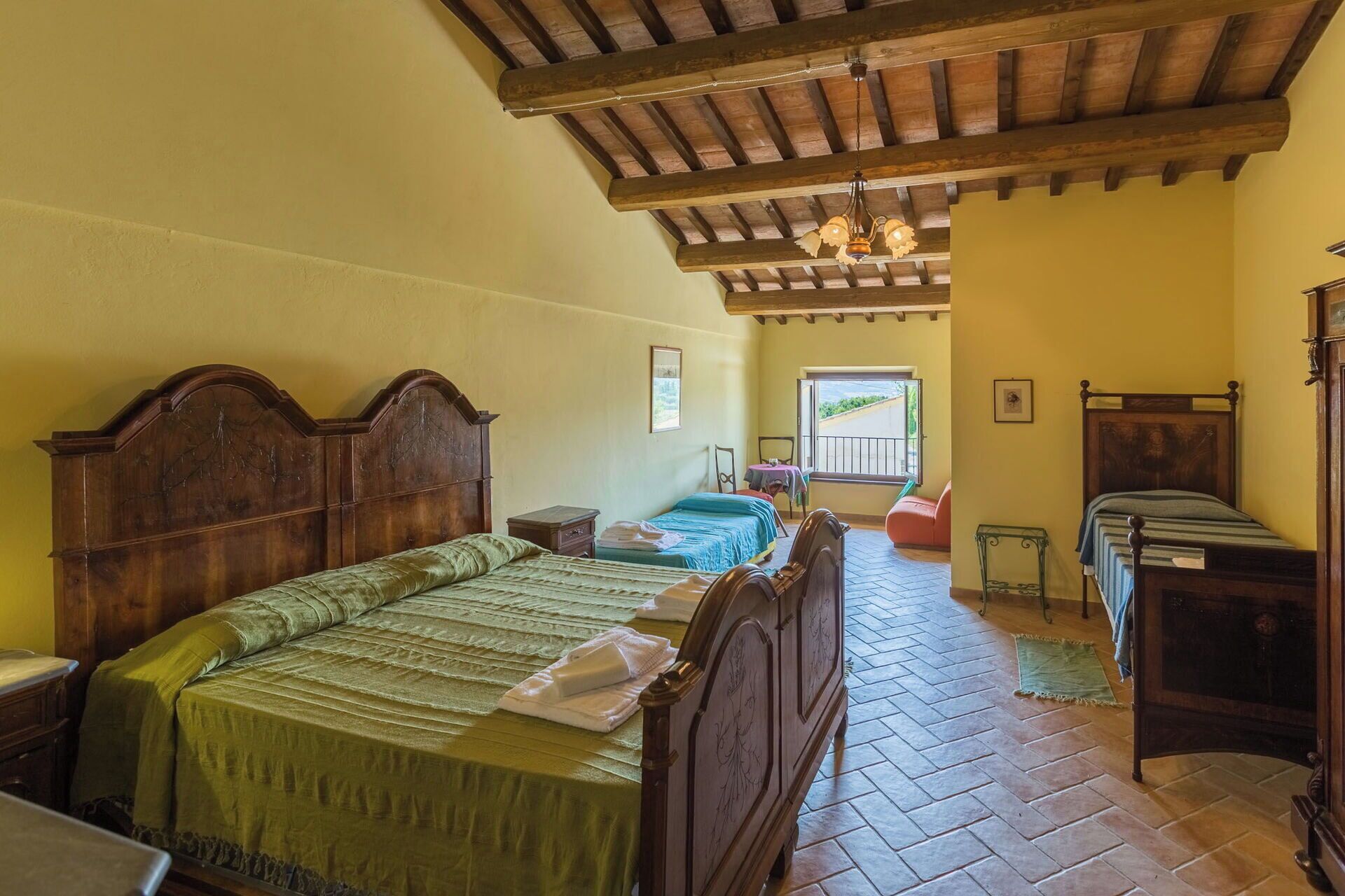 Quarto tradicional com cama e cómoda de madeira, e varanda com vista.