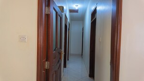 Un pasillo estrecho con puertas de madera a ambos lados, un interruptor de luz en la pared izquierda y una lámpara en el techo.