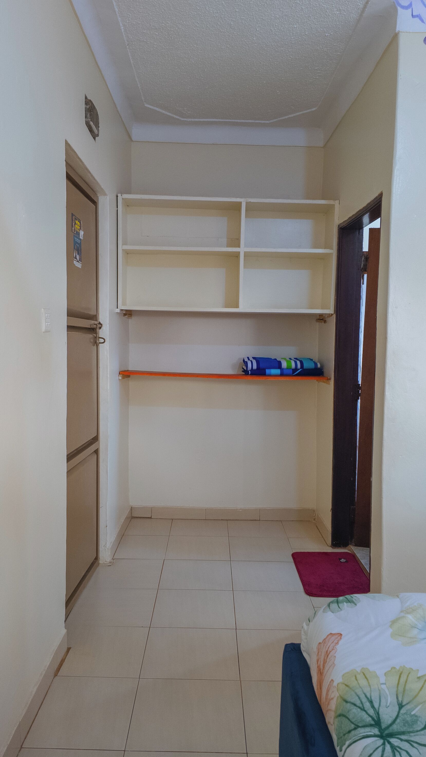 Une petite pièce, de taille modeste, comprenant un lit, une étagère et une porte.
