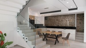 A modern kitchen with a stone backsplash, a dining area with a wooden table and chairs, and a glass staircase leading to another level. - O-Cyanea Villa: Luxurious 4-Bedroom Retreat with Heated Pool in Kournas (Paralia Kourna)