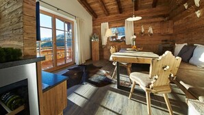 Ein rustikales Blockhaus-Interieur mit einem Holzespeisesaal, Stühlen, einer Couch und einem großen Fenster mit Blick ins Freie.