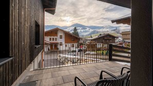 Un balcone con vista su un paesaggio montano, un edificio in legno e un'area pavimentata con una recinzione.