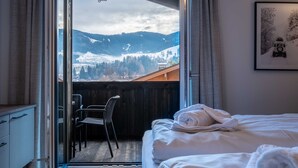 Une chambre à coucher avec un lit, une chaise et une vue sur les montagnes, visible à travers une porte vitrée.