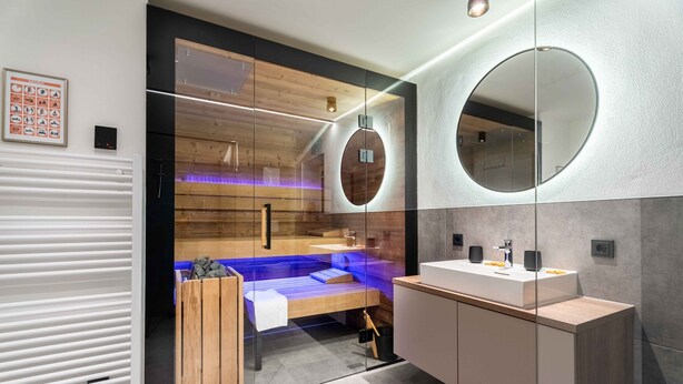 Une salle de bain moderne avec une cloison en verre, des éléments décoratifs en bois, un miroir rond et un banc intégré.