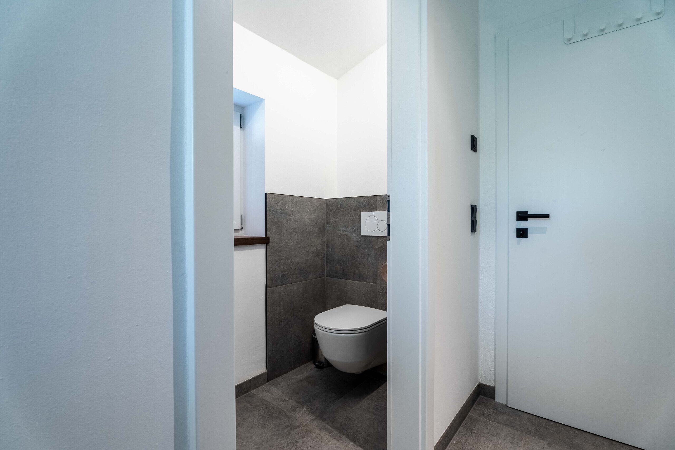 Un pasillo estrecho que conduce a un baño con inodoro, paredes de azulejos y una puerta blanca.