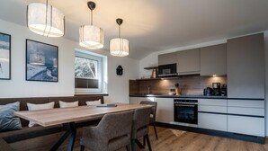 Une cuisine moderne avec une table à manger en bois, des chaises grises, des luminaires suspendus et un four encastré.