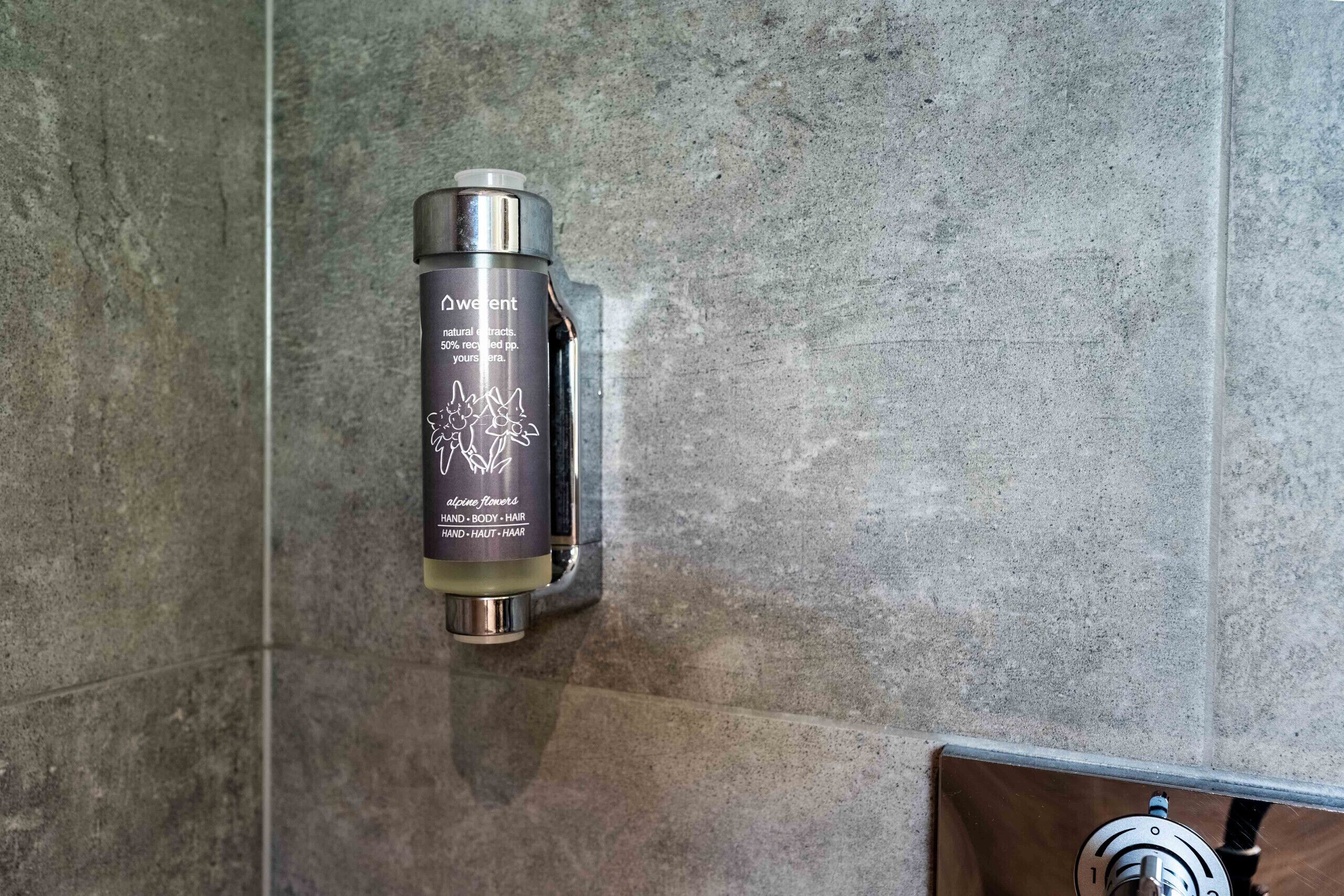 Un baño con dispensador montado en la pared, etiquetado 'Dewent', y un grifo metálico.