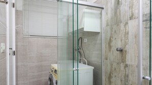 A modern bathroom with a glass shower enclosure, a built-in washing machine, and a tiled floor. - Premium RJ - Consulado (Rio de Janeiro)