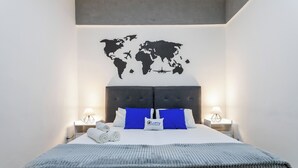 A neatly made bed with a world map on the wall, a grey headboard, and two bedside lamps. - Premium RJ - Consulado (Rio de Janeiro)