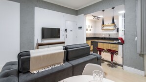 A modern living room with a grey sofa, a TV, and a dining area with a table and chairs. - Premium RJ - Consulado (Rio de Janeiro)