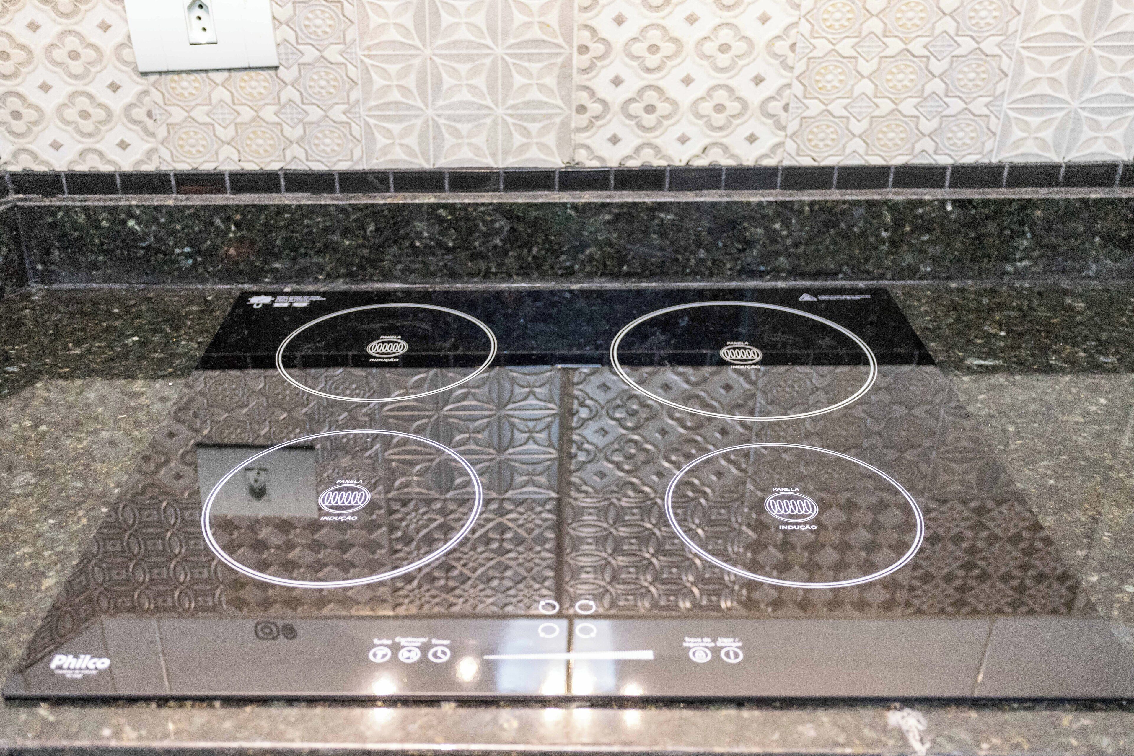 A kitchen with a Philco induction cooktop, patterned backsplash, and a black granite countertop.