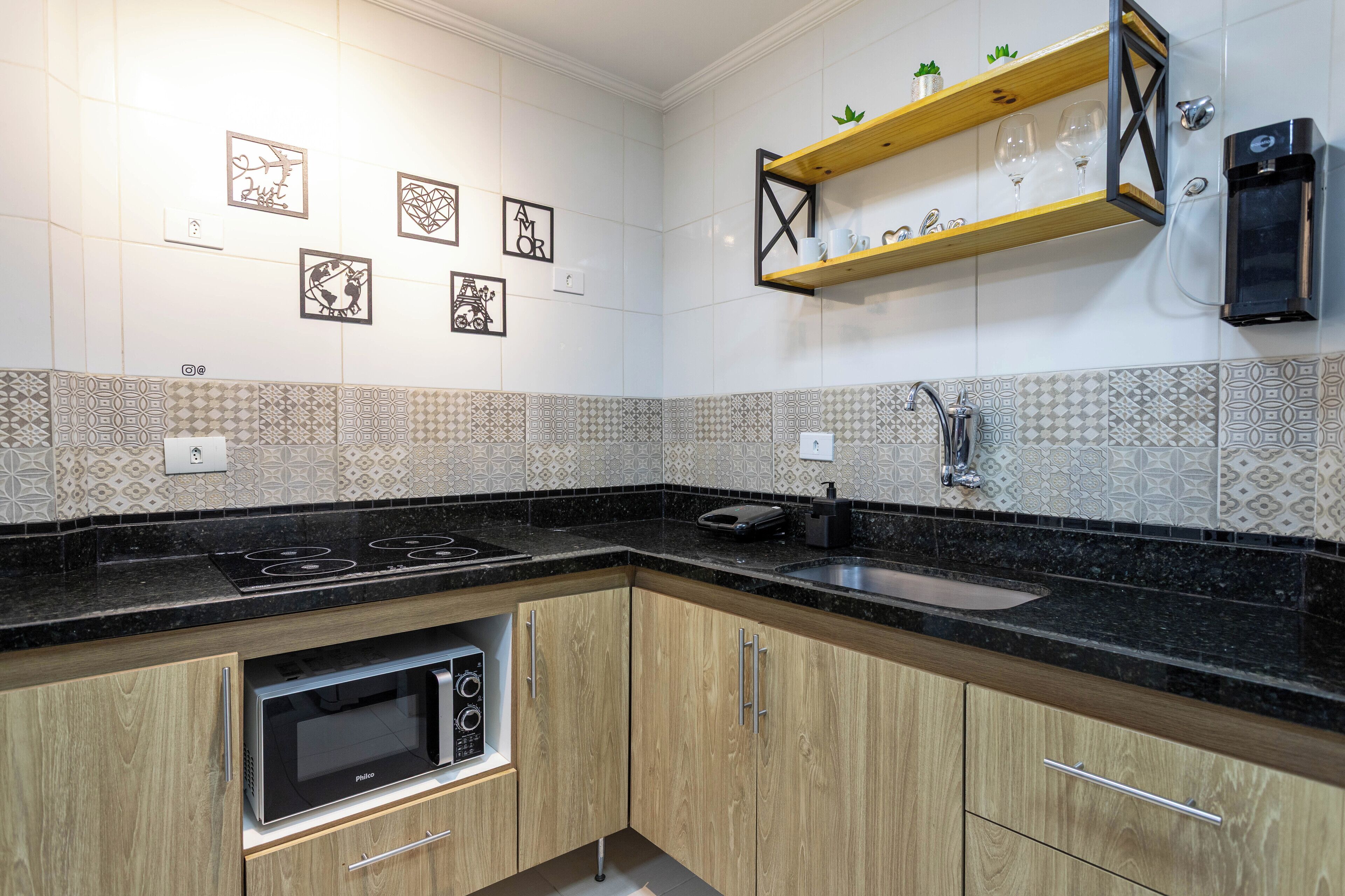 Een keuken met een zwart aanrecht, houten kastjes, een ingebouwde magnetron, een spoelbak en decoratieve muurdecoratie.
