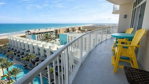 Ein Balkon mit gelben Stühlen, einem Pool und Blick auf Strand und Meer.