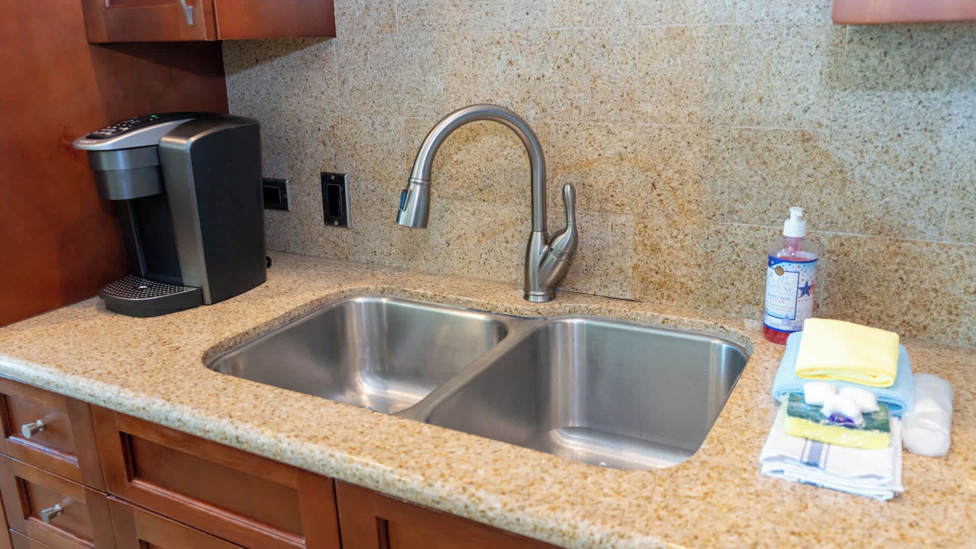 A kitchen with a double stainless steel sink, a coffee maker, and a bottle of hand soap.