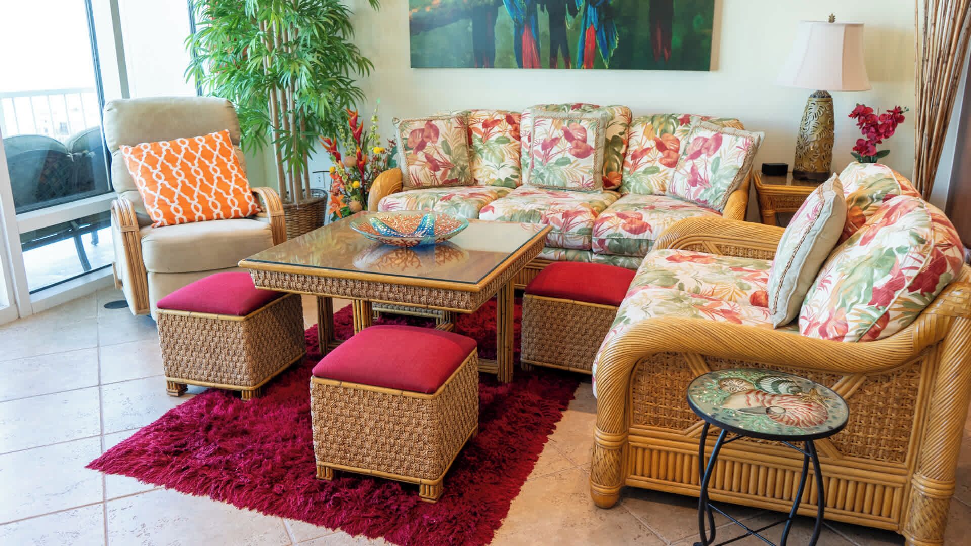 A living room with wicker furniture, a glass coffee table, and a red shag rug.