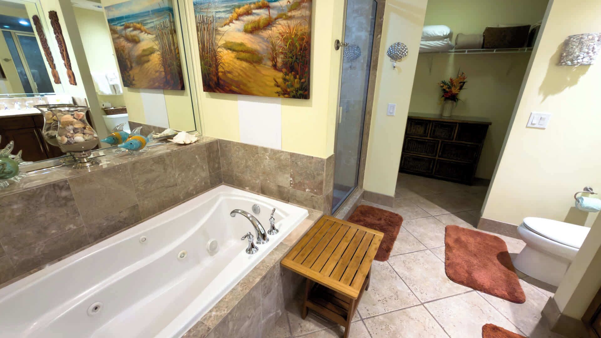 Une salle de bain avec une grande baignoire, un tabouret en bois, des toilettes et un lavabo.