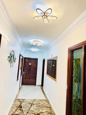 A hallway with a patterned floor, a ceiling light fixture, and framed artwork on the walls. - Fortune Home Service Apartment, Studio E-30 (New Delhi)