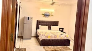Quarto com cama, ventilador de teto, luminária na parede e geladeira.