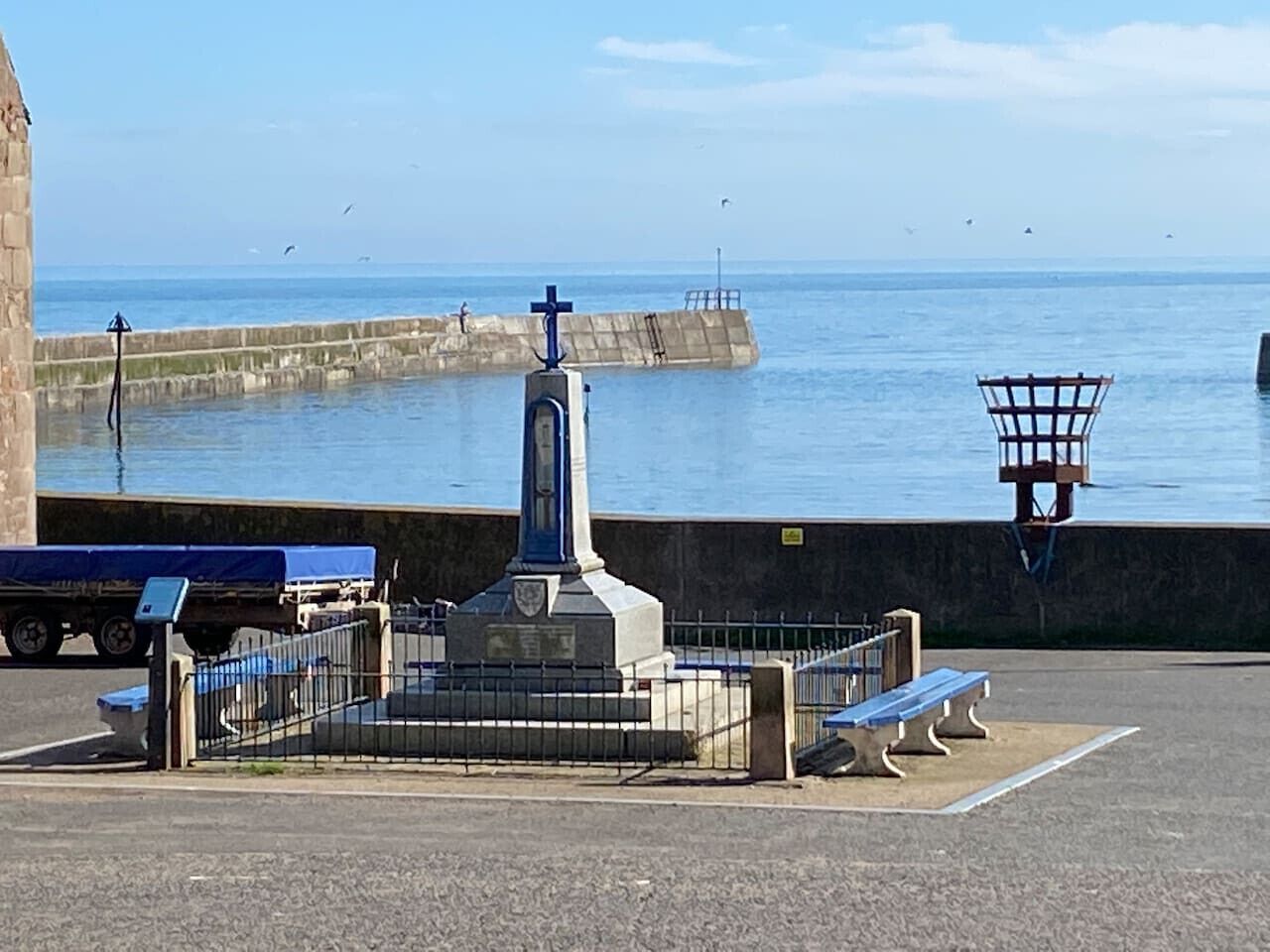 Ein Gedenkdenkmal mit einem Kreuz, umgeben von einem Zaun, Bänken und einem Rettungsring.