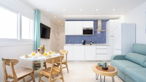 Una cucina moderna con mobili bianchi, una parete protettiva blu e un'area pranzo con sedie di legno e un tavolo rotondo.