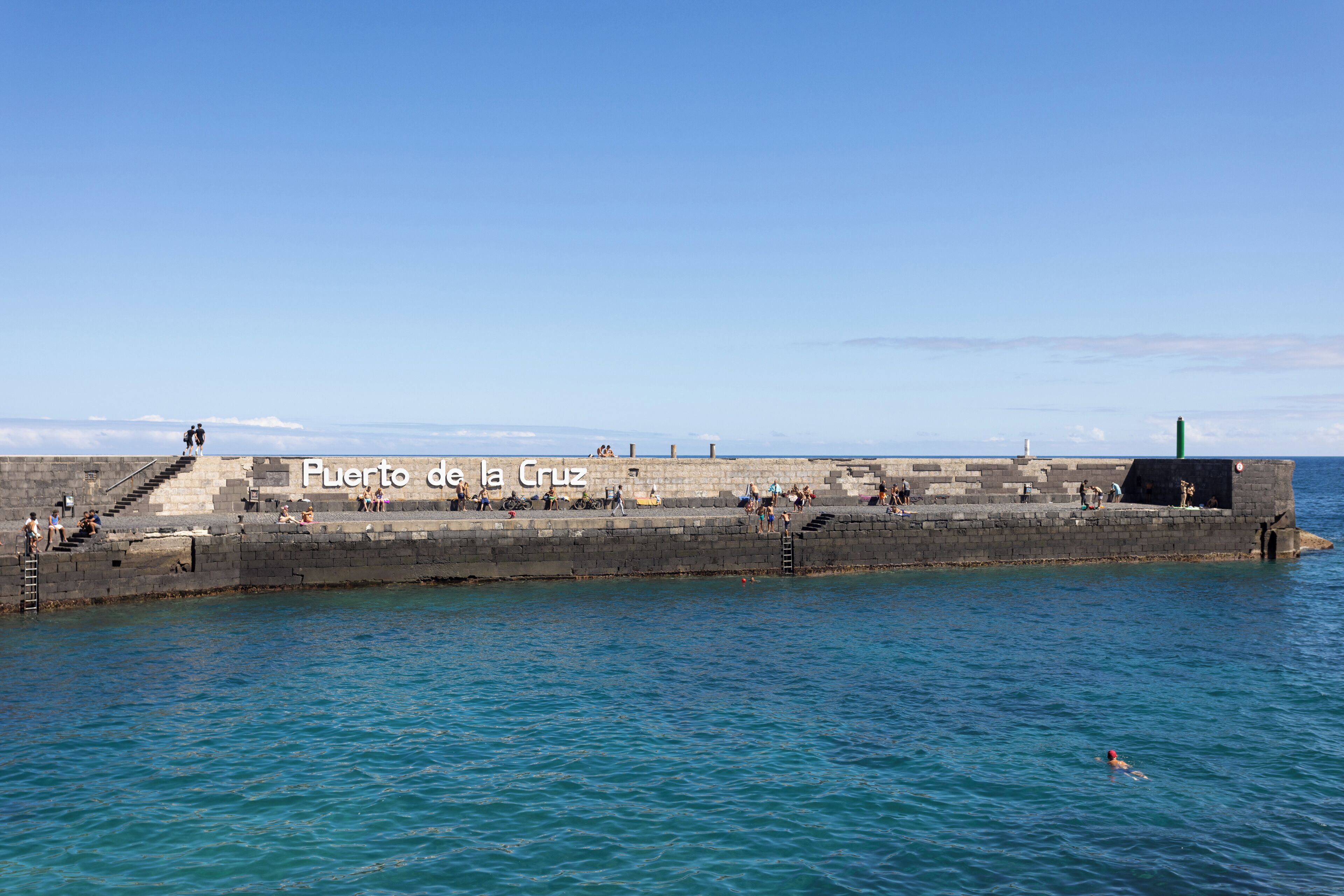 A pier with the text "Puerto de la Cruz" and people walking along it.