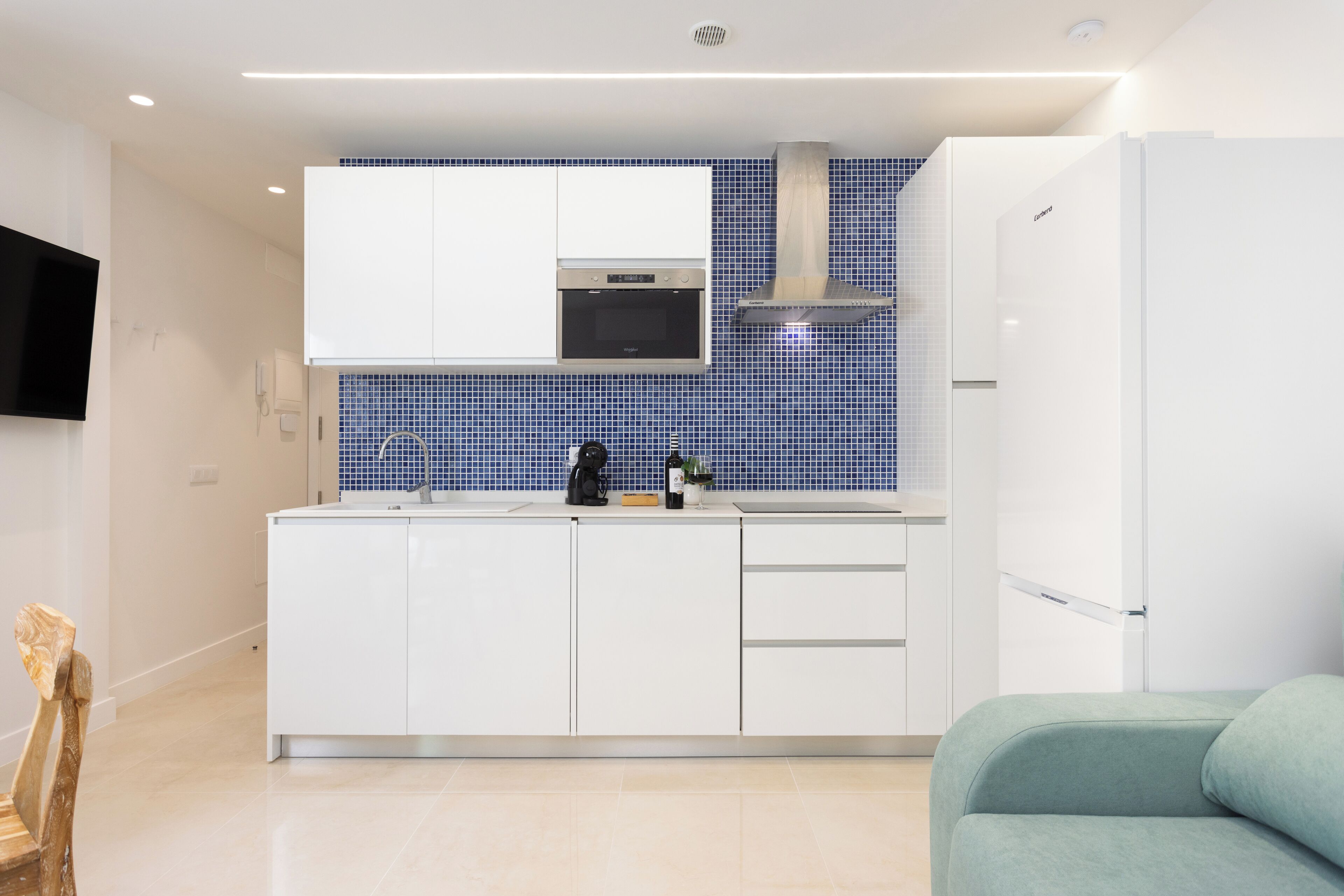 A modern kitchen with white cabinets, a blue tiled backsplash, and a built-in oven.