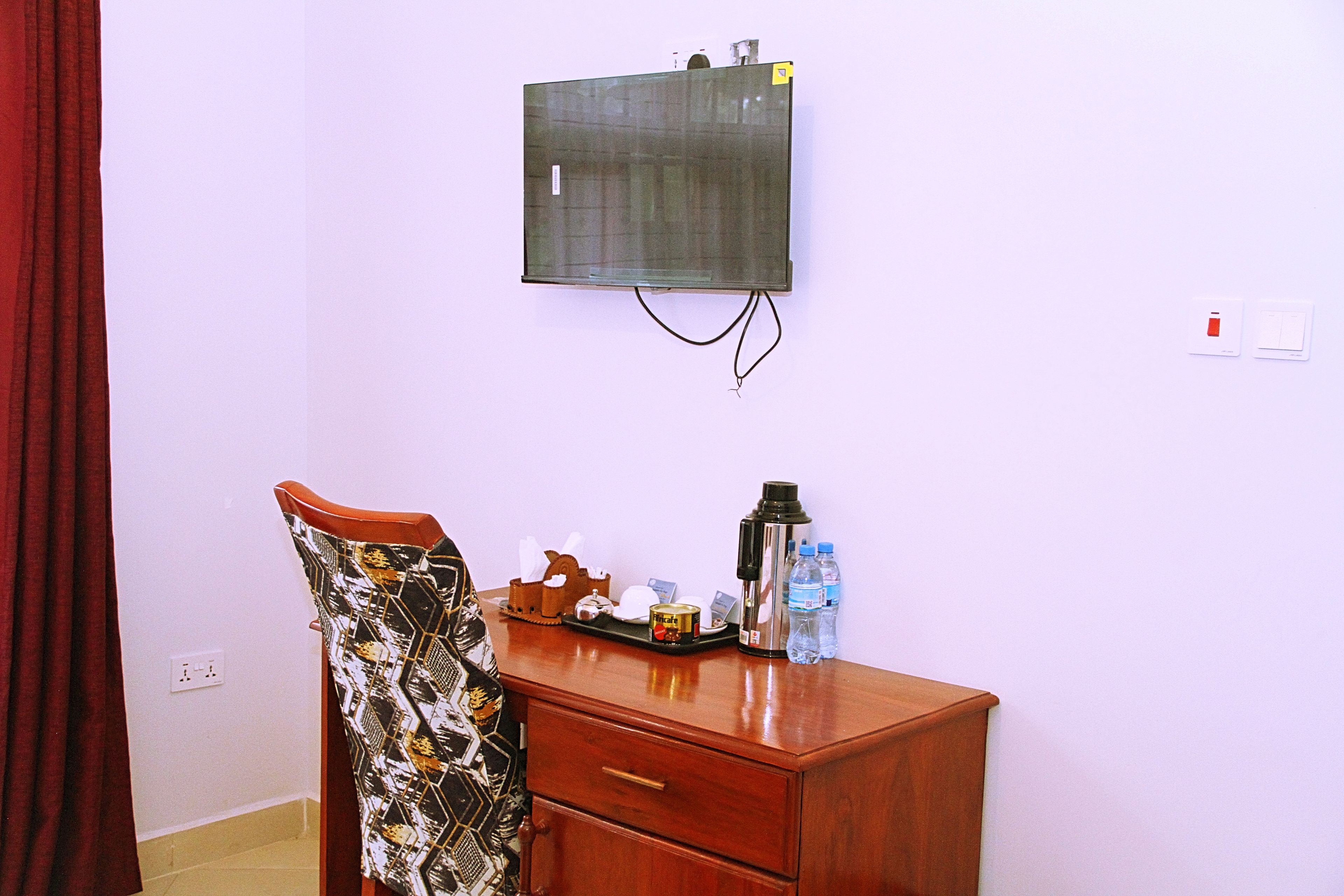 Una habitación con un escritorio de madera, una silla, un televisor de pared y un enchufe.