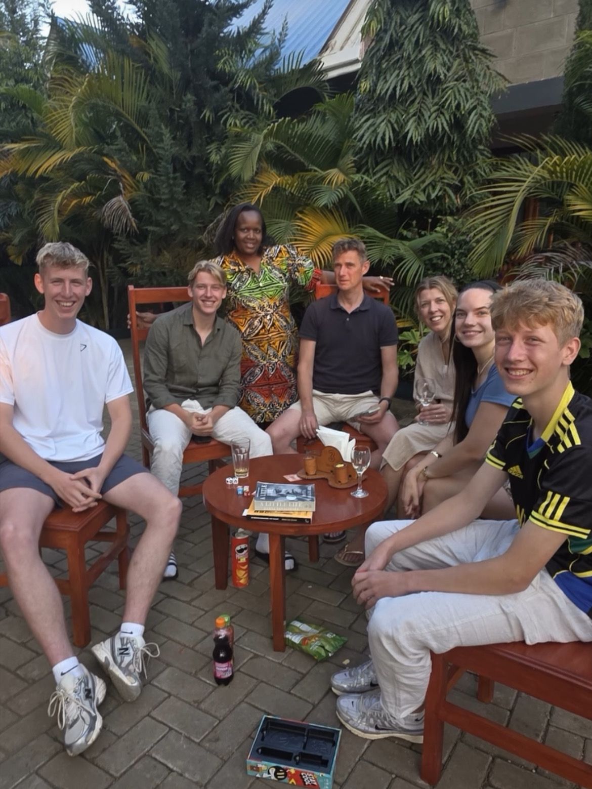 Un grupo de personas sentadas alrededor de una mesa redonda al aire libre, con un paisaje tropical de fondo.