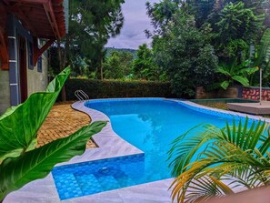 A swimming pool with a tiled edge, surrounded by greenery and a wooden deck. - VIGO LODGE (Arusha)