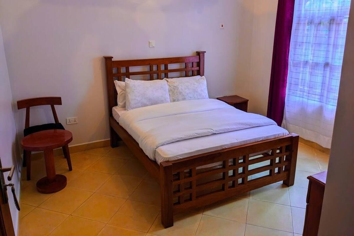 Un dormitorio con una cama de madera, una mesita redonda pequeña y una silla.