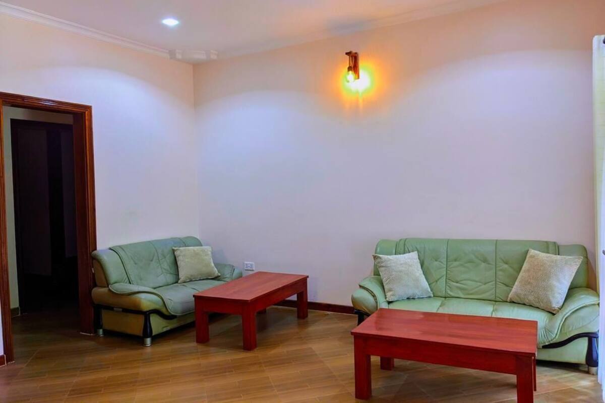 Una sala de estar con dos sofás verdes, una mesa de centro de madera y una lámpara fijada a la pared.