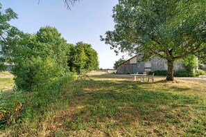 Un espace extérieur verdoyant avec un arbre, une table de pique-nique et un bâtiment en arrière-plan.