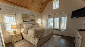 A bedroom with a wooden ceiling, a large bed with beige bedding, a nightstand with a lamp, and a dresser. - Spacious 4-bedroom farmhouse in beautiful Appling with AC (Appling)