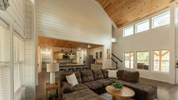 A spacious living area with a large sectional sofa, a round coffee table, and a view of the kitchen and dining area through an open archway. - Spacious 4-bedroom farmhouse in beautiful Appling with AC (Appling)