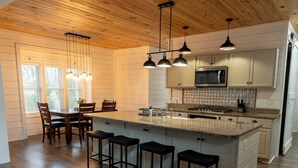 A modern kitchen with a wooden ceiling, a central island with bar stools, and a dining area with a table and chairs. - Spacious 4-bedroom farmhouse in beautiful Appling with AC (Appling)