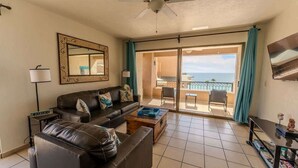 A living room with a sofa, coffee table, and a television. There is a balcony with a view of the ocean. - Sonoran Spa N 501 1 Bed 1 Bath (Puerto Peñasco)